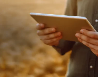 Imagem de pessoa interagindo com tablet, ao fundo está o campo.