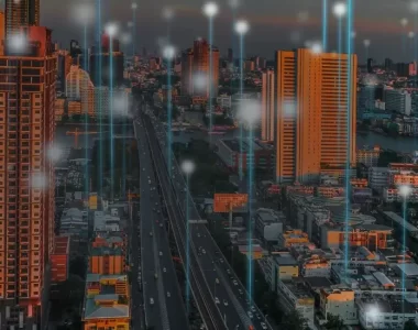 Imagem de cidade com grandes prédios e feixes de luz, que ilustram conexão, indo em direção ao céu